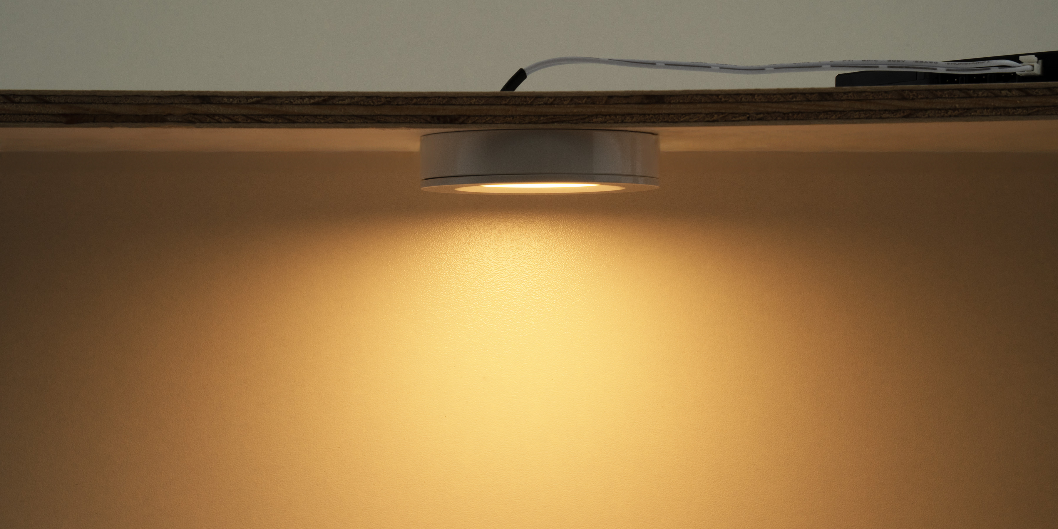 LED Aufbauleuchte unter einem Regal montiert mit warmem Licht fuer gezielte Beleuchtung