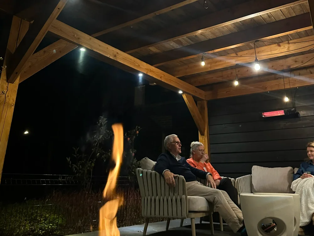 Warme Aussenbeleuchtung unter einer Holzterrasse mit Feuerstelle, Sitzecke und gemuetlicher Abendstimmung