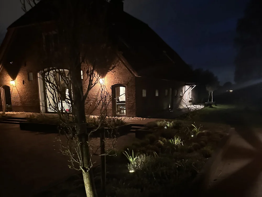 Stimmungsvolle Gartenbeleuchtung an einem Landhaus mit beleuchteter Fassade, Pflanzen und Weg am Abend