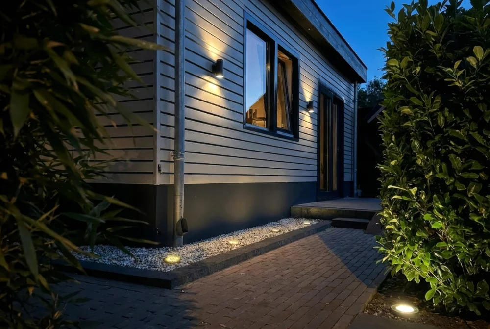 Aussenwandleuchten an Fassade und Gartenweg geben warmes Licht und machen den Eingang uebersichtlich