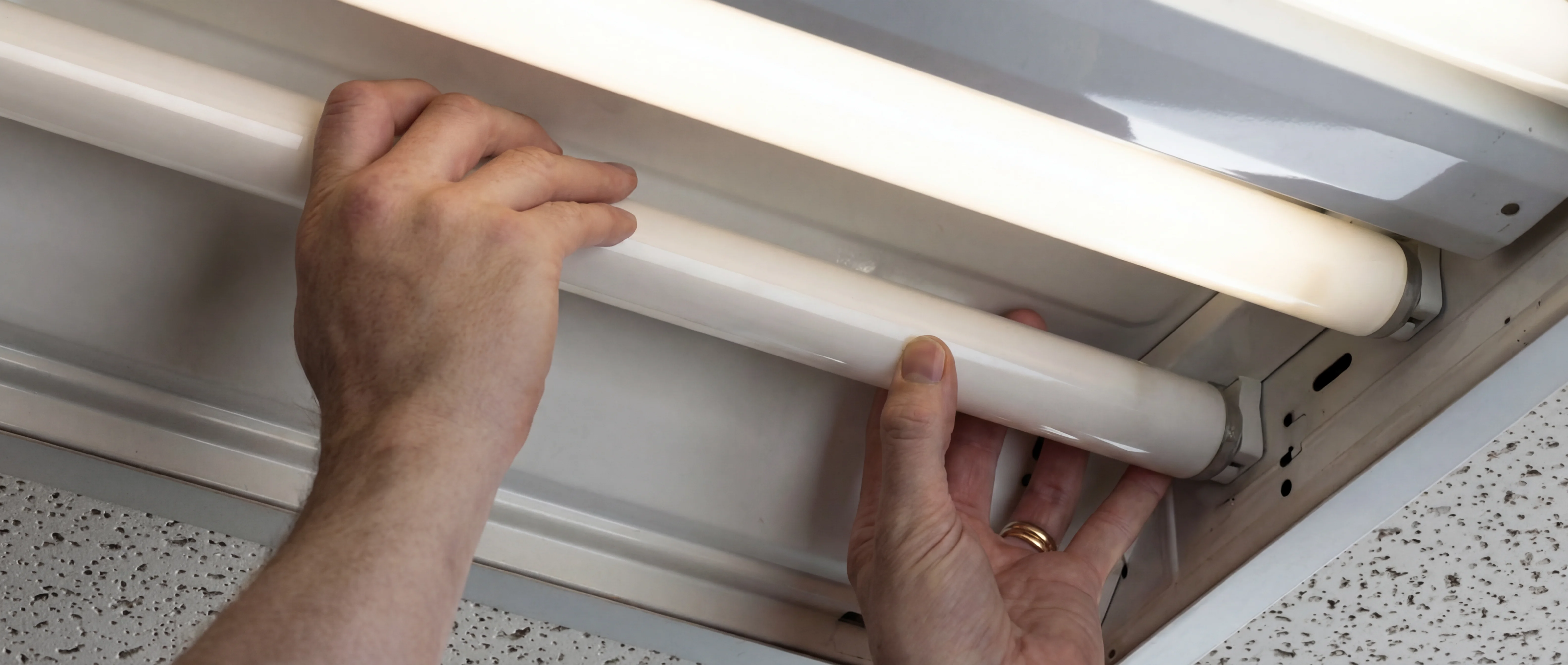 Handen vervangen een TL-buis in een plafondarmatuur door LED-verlichting
