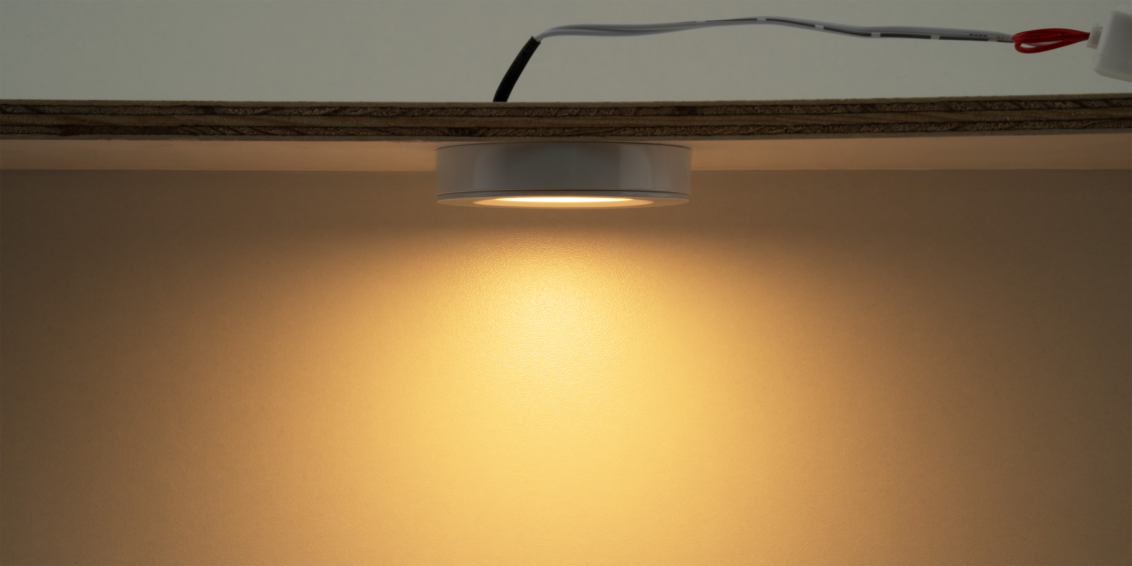 Mini LED Aufbauleuchte unter einem Regal montiert mit warmem Licht fuer gezielte Beleuchtung