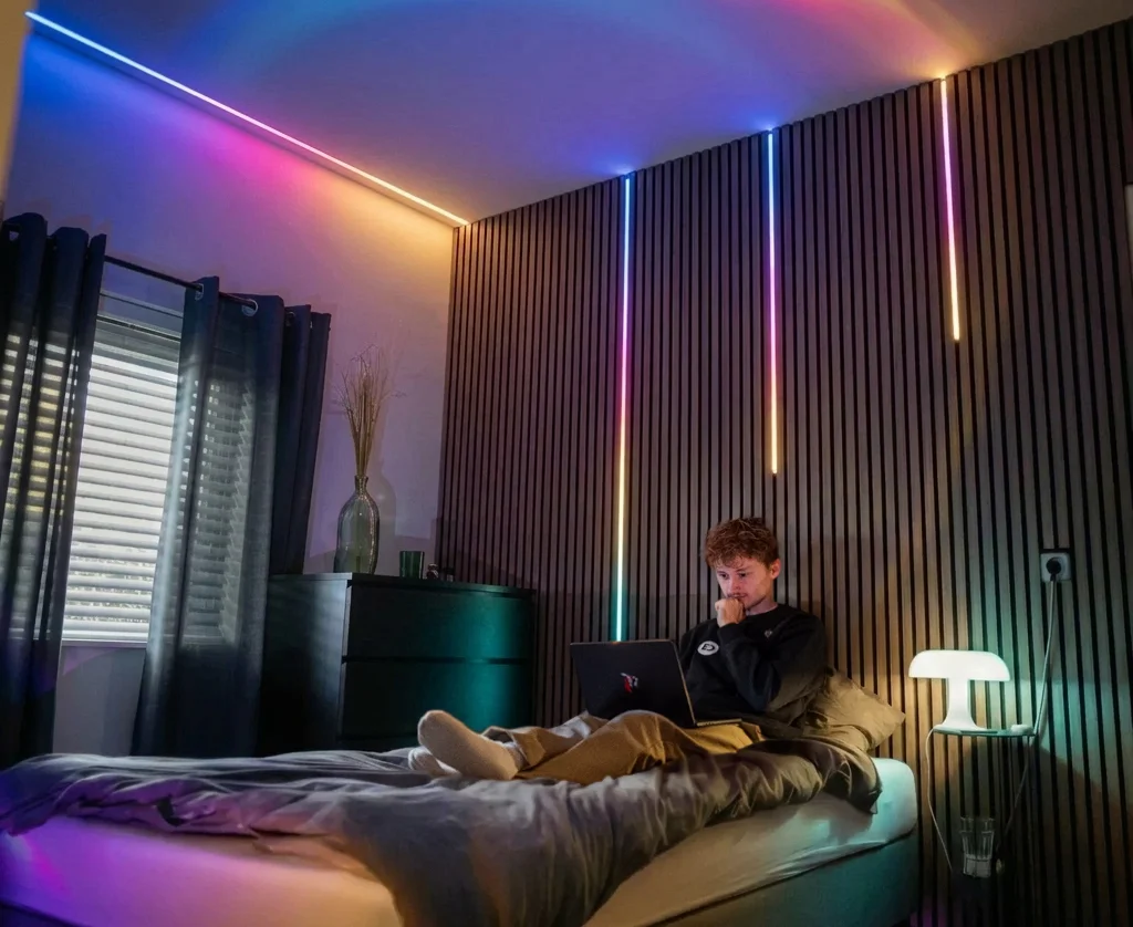 Schlafzimmer mit RGBWW LED-Streifen an Decke und Wandpaneelen fuer farbenfrohe Beleuchtung.